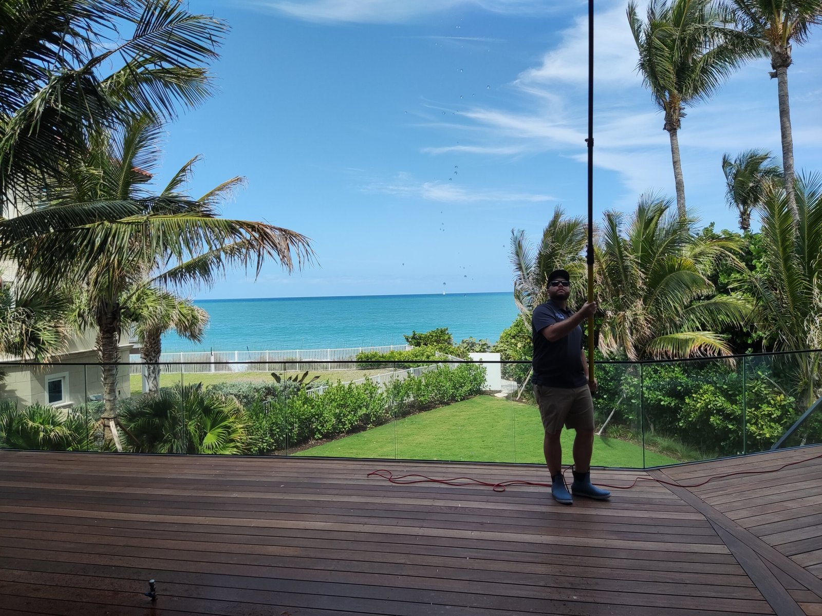 Professional window cleaner using pure water system on a luxury home in Sebastian, FL with ocean view in the background.