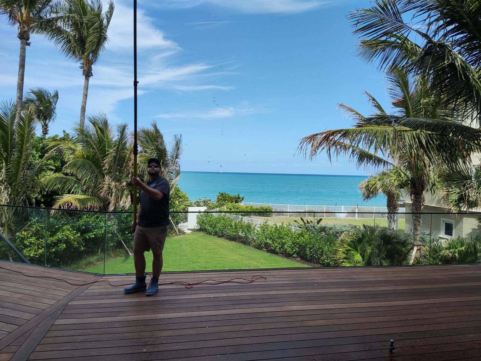Professional window cleaner using pure water system on a luxury home in Sebastian, FL with ocean view in the background.